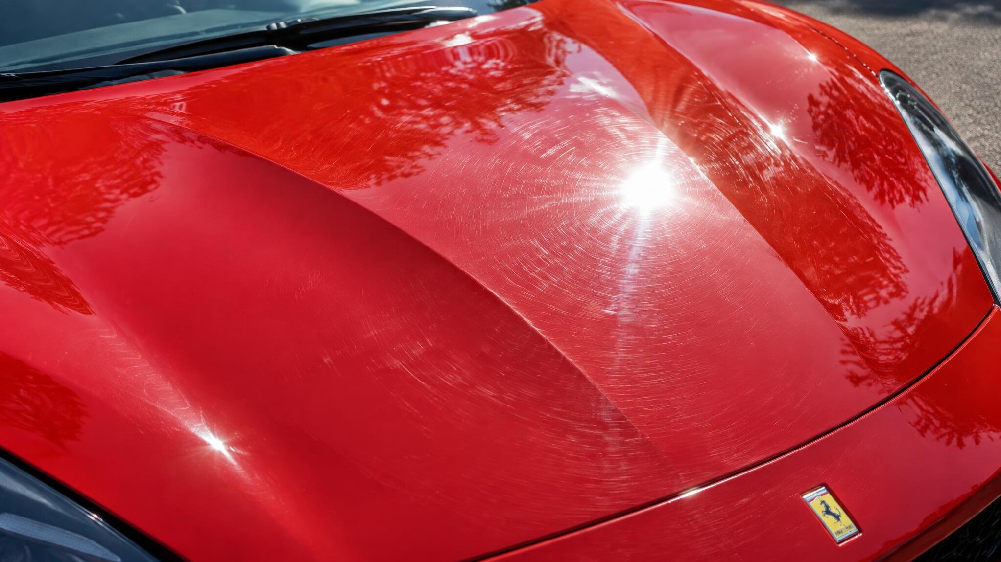 Red sports car hood with reflections showing swirl marks