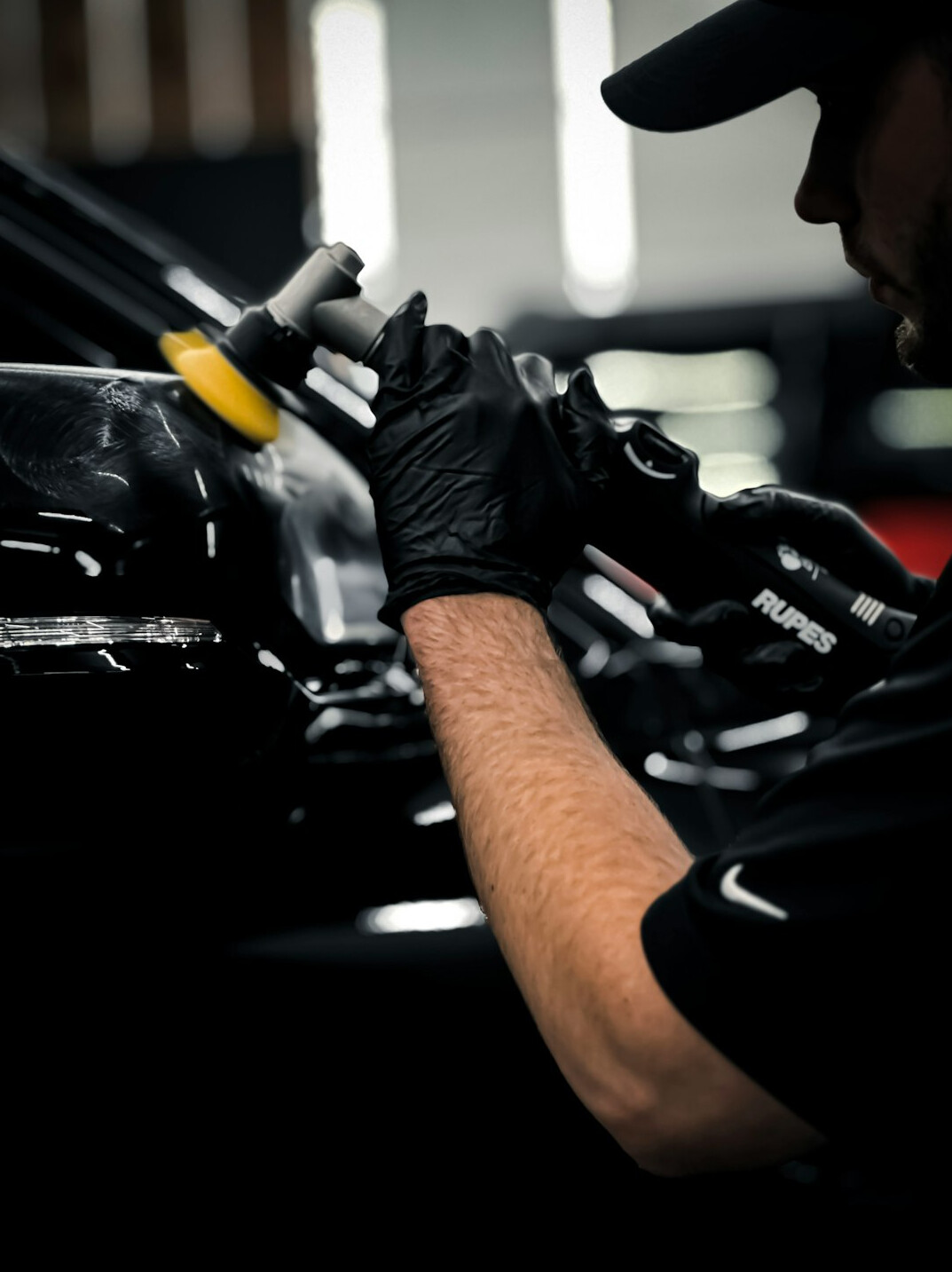 Technician polishing a car body panel with a machine polisher